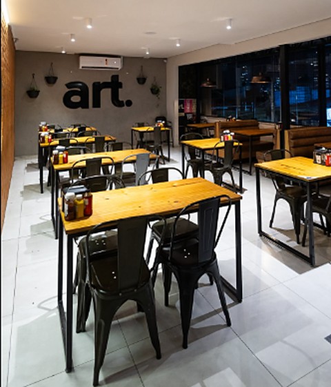 O salão do Artesanos Burger, com mesas de madeira e o 'art.' na parede
